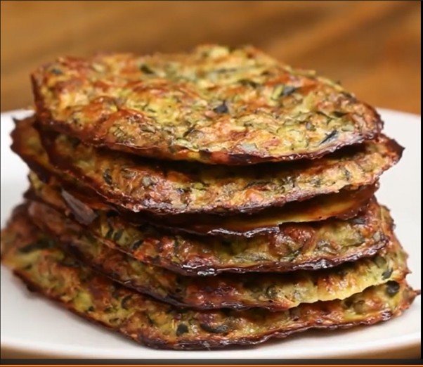 Stack of crispy veggie fritters on a white plate, golden brown with visible greens and herbs inside